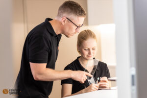 Andreas Speckert zeigt Mitarbeiterin das bearbeiten von maßgefertigten Ohrstücken